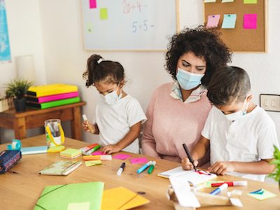 Teacher draws with children while wearing surgical face mask for coronavirus - School and safety measures